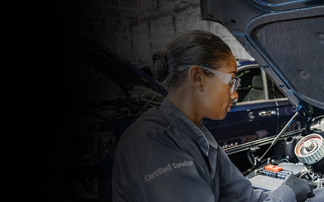 GMC Certified Service Technician Using a Tool to Inspect a Vehicle's Engine Bay