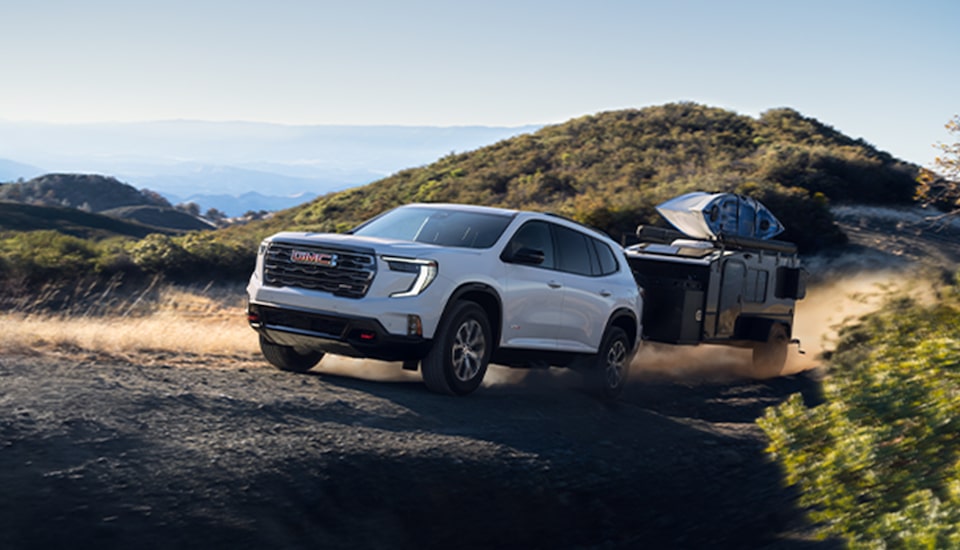 A White GMC SUV Towing a Camper On a Trail