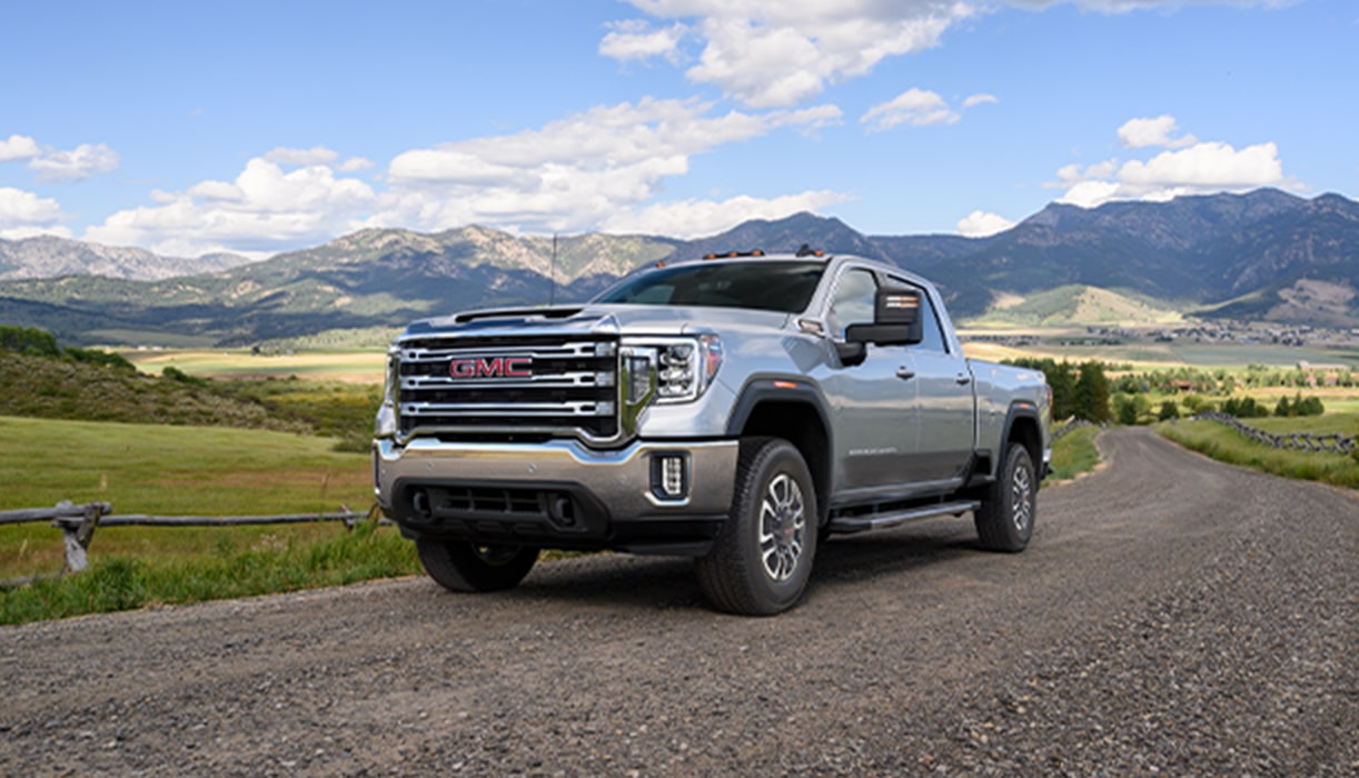 GMC Truck Driving on Gravel Road with Snow Covered Mountains in Background