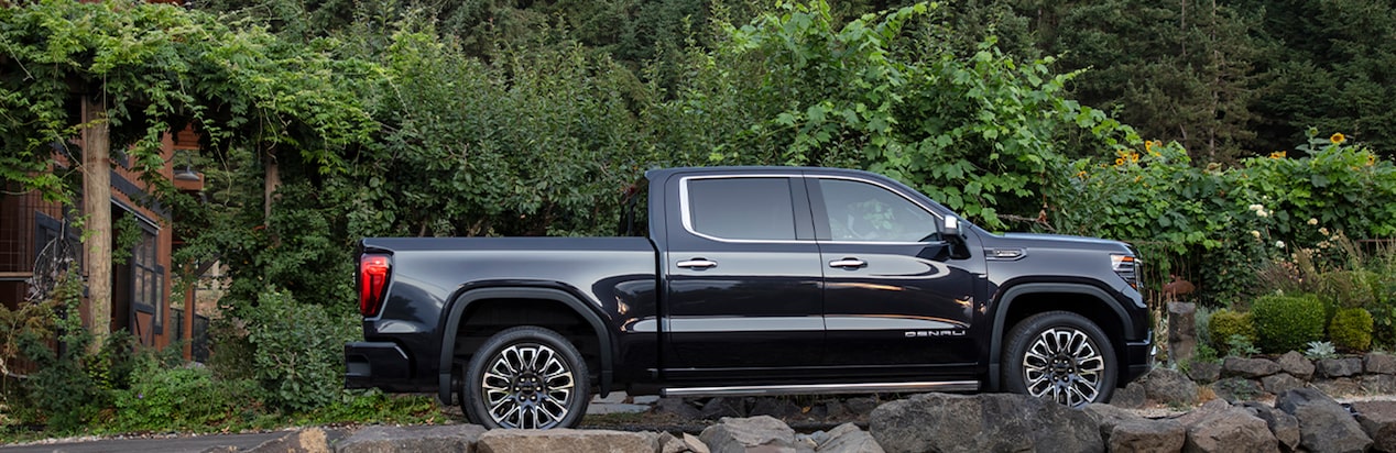 A Side View of a Black GMC Truck Parked In Front Of an Ivy-Covered Fence