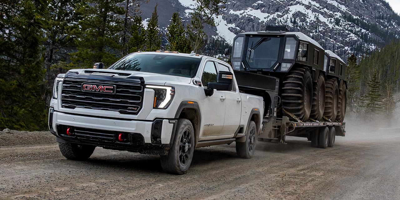 The GMC Sierra HD Truck Driving Down a Dirt Road in the Mountains While Towing a Trailer