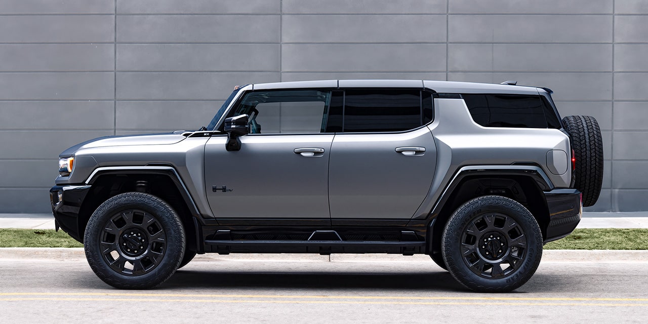 Front Three-Quarter View of the GMC HUMMER EV Pickup Truck Driving Down a Dirt Road with Mountains in the Background