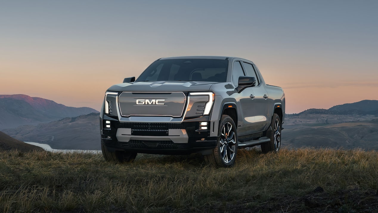 Three-Quarters Front View of a GMC Sierra EV Parked on a Grassy Hill at Sunset
