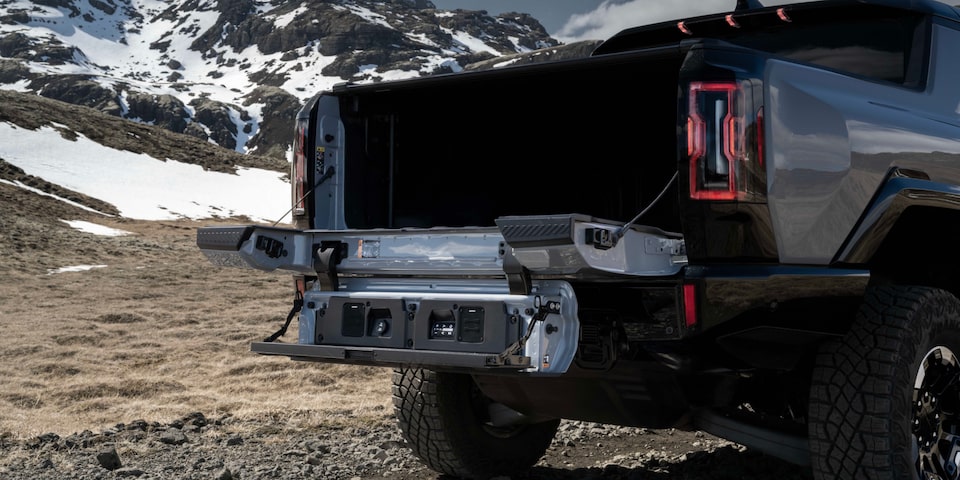 Rear End View of the 2025 Hummer EV Pickup Truck's MultiPro Tailgate Opened Overlooking Snowy Mountains