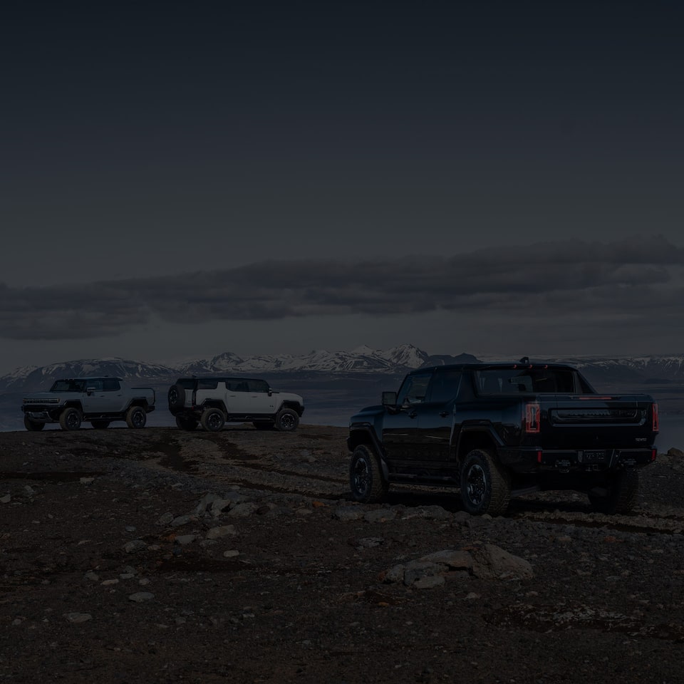 Three GMC Hummer EV SUVs Parked on a Rocky Road Overlooking a Mountain View