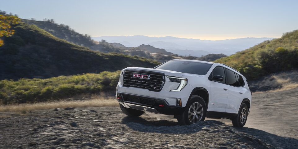 The GMC Acadia AT4 Mid-Size Off-Road SUV Driving Over Rough Terrain with a Mountain View in the Background