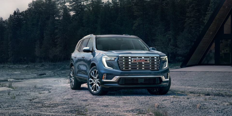 The GMC Acadia Denali Luxury Mid-Size SUV Parked on a Beach with a Forest View in the Background