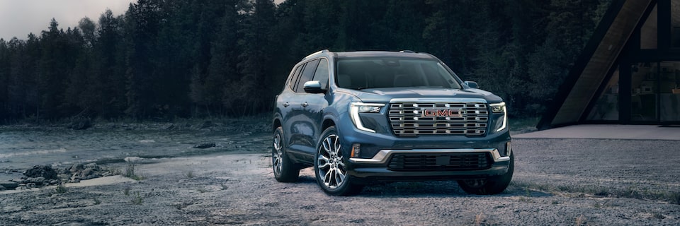 The GMC Acadia Denali Luxury Mid-Size SUV Parked on a Beach with a Forest View in the Background