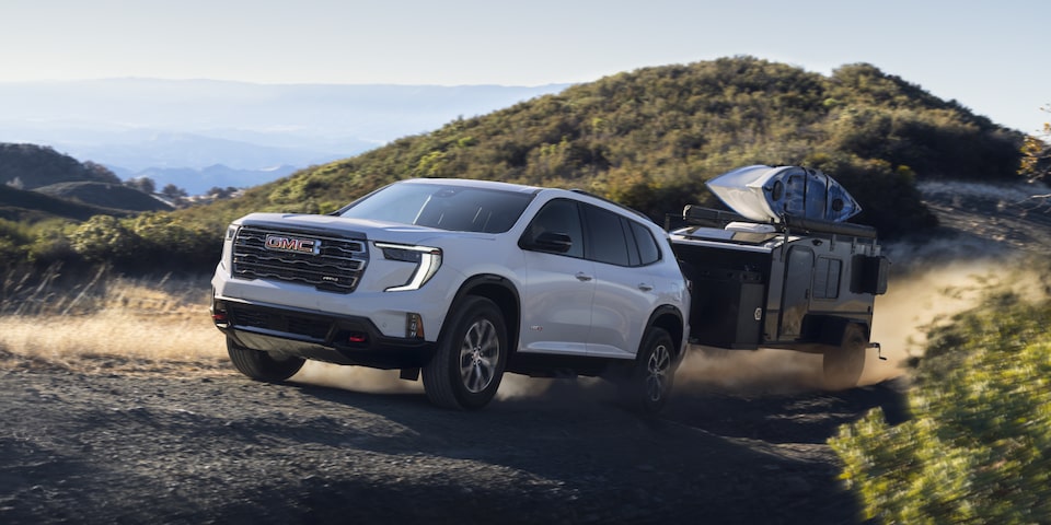 A White GMC Acadia Towing a Trailer Off-Road