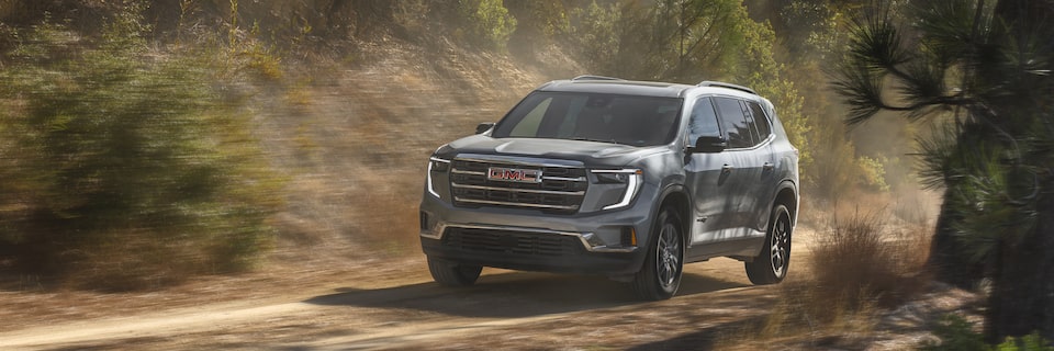 The GMC Acadia Mid-Size SUV Driving Down a Dirt Road Through the Forest Kicking up Dust
