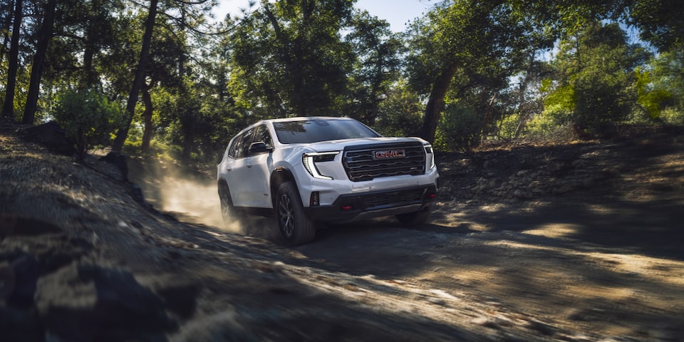 The 2025 GMC Acadia Mid-Size SUV Driving on a Dirt Road Through the Woods Kicking up Dust