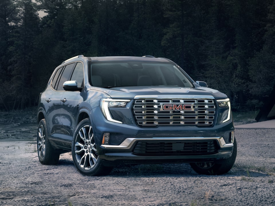 The GMC Acadia Denali Luxury Mid-Size SUV  Parked on a Beach with a Forest View in the Background