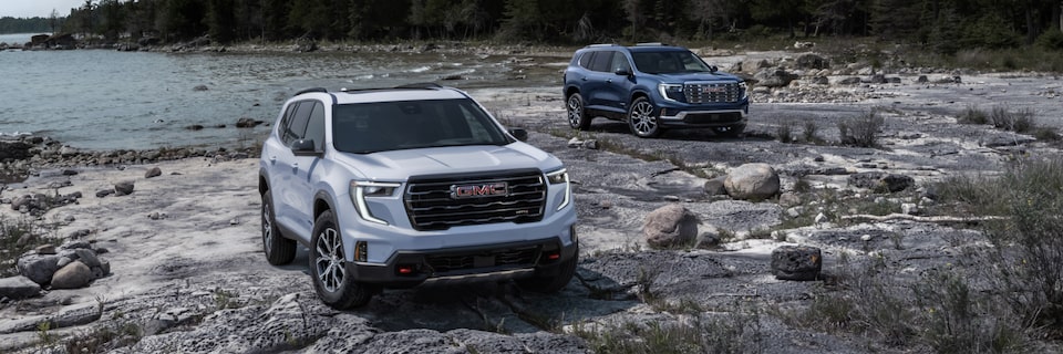 Two 2025 GMC Acadia Mid-Size SUVs Parked at the Beach with a Forest in the Distance