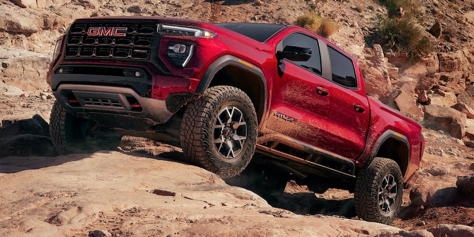 A Red 2025 GMC Canyon AT4 Driving Uphill Off-Road on Rocks