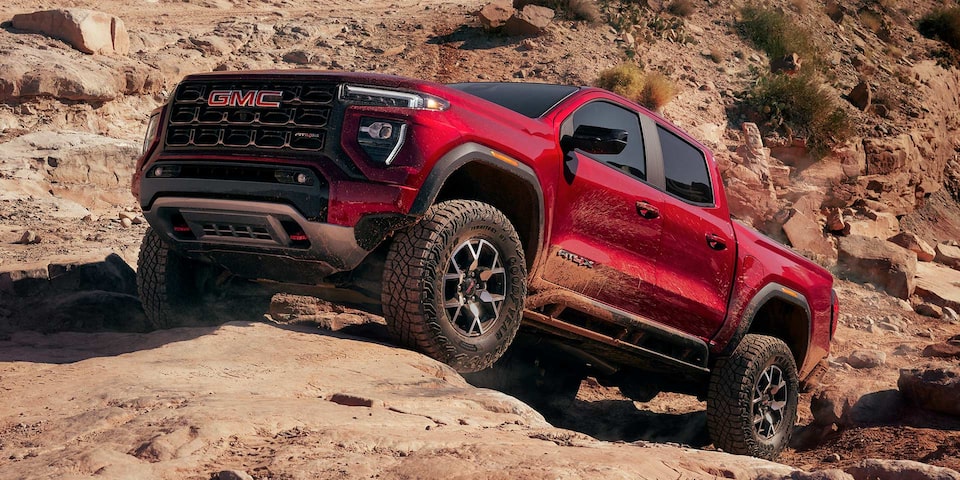 A Red 2025 GMC Canyon AT4 Driving Uphill Off-Road on Rocks