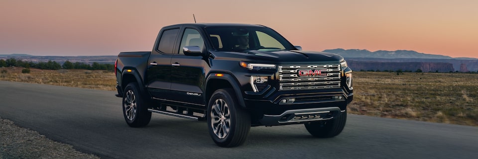 A Black 2025 GMC Canyon Denali Driving Down a Road During a Sunset