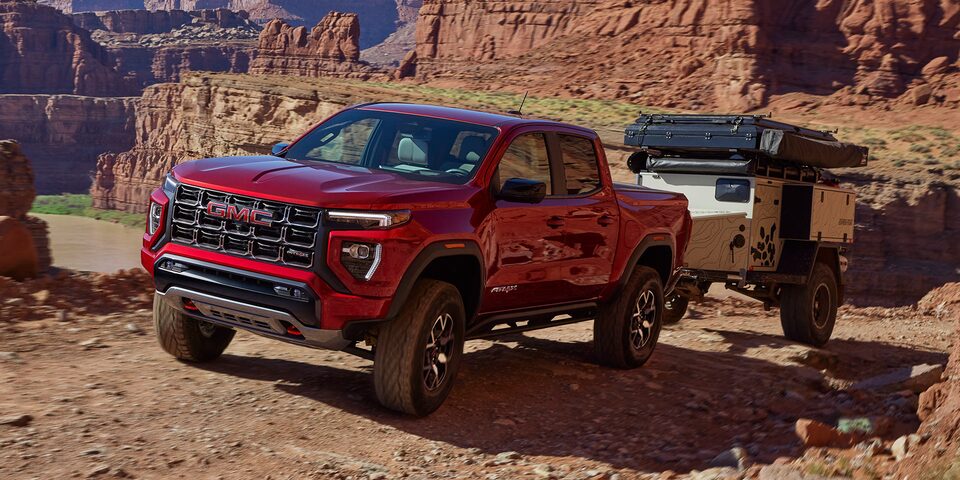 Three-quarter View of a Red 2025 GMC Canyon Hauling a Trailer Through the Canyon Desert