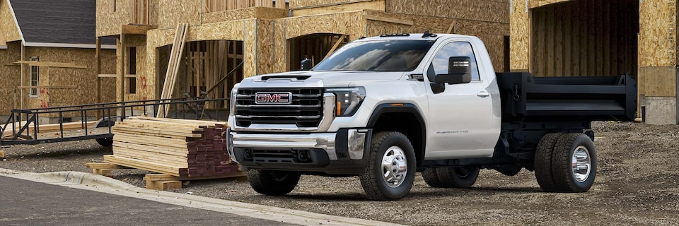 Wide Front Three-Quarters View of a 2025 GMC Sierra HD Chassis Cab Truck Parked in Front of a House Under Construction