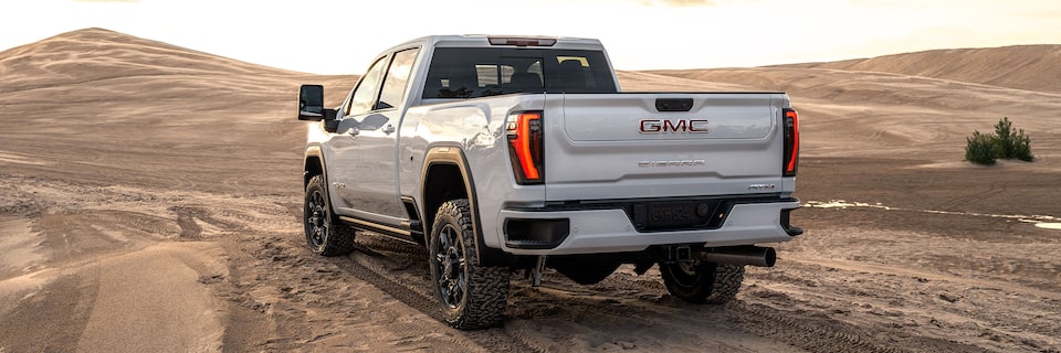 Wide Rear Three-Quarters View of a 2025 GMC Sierra HD AT4 Truck Driving Through the Desert