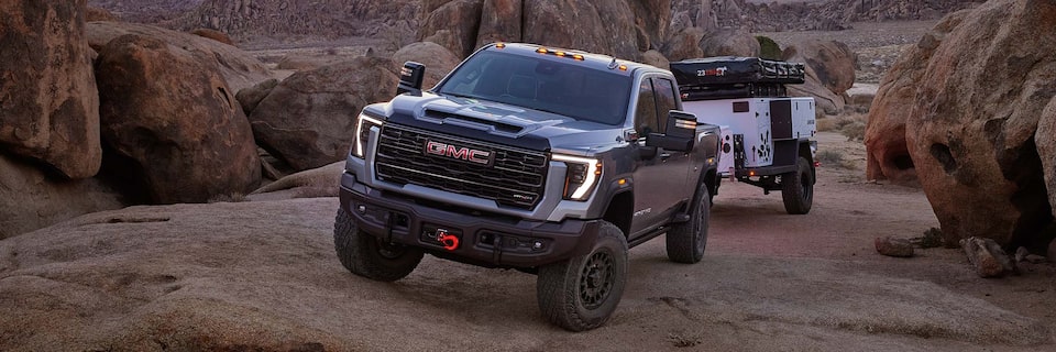 Wide View of a 2025 GMC Sierra HD AT4 Truck Hauling a Trailer Through Rocky Terrain at Dusk