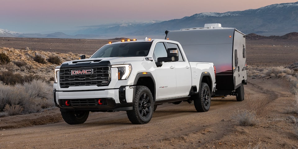 A 2025 GMC Sierra HD AT4 Truck Hauling a Trailer Through the Desert at Dusk
