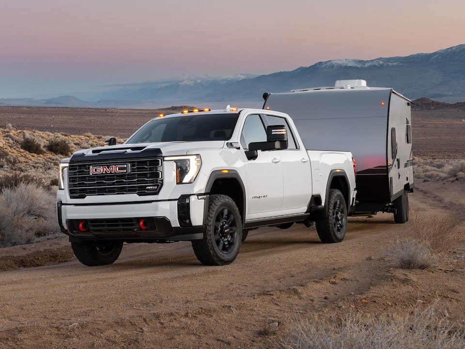 A White GMC Sierra HD Driving Off-Road Towing a Trailer