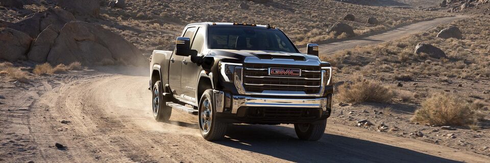 Wide Front Three-Quarters View of a 2025 GMC Sierra HD Truck Driving Through the Desert