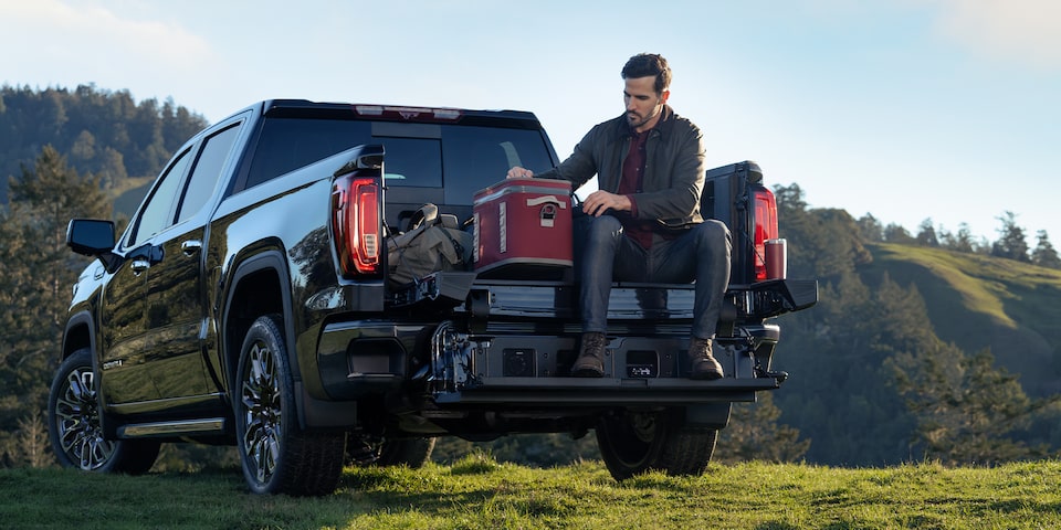 The GMC Sierra 1500 Denali Pickup Truck Parked Off-Road While a Man sits on the MultiPro Tailgate
