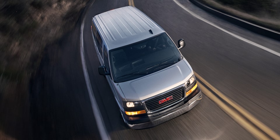 Birdseye Three-Quarters View of a 2025 GMC Savana Passenger Van Driving on an Empty Road at Night