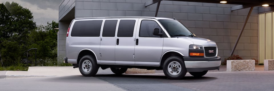 Wide Front Three-Quarters View of a 2025 GMC Savana Passenger Van with a Building in the Background