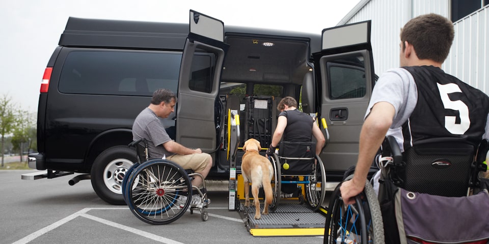 A Person in a Wheelchair Using the Lift Feature on the 2025 GMC Savana Passenger Van with a Dog by His Side