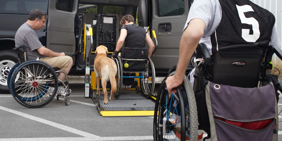 A Person in a Wheelchair Using the Lift Feature on the 2025 GMC Savana Passenger Van with a Dog by His Side