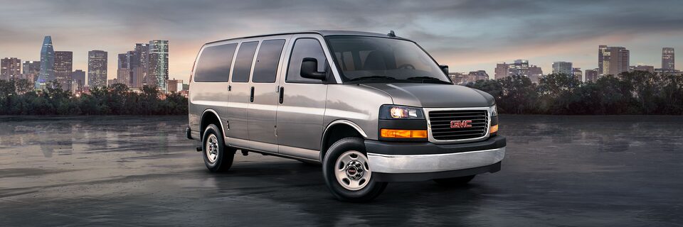 Wide Front Three-Quarters View of a 2025 GMC Savana Passenger Van with a City in the Background