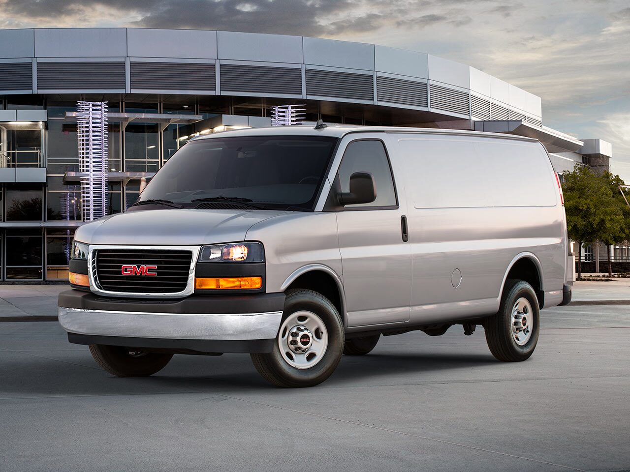 Front Three-Quarter View of a Silver 2026 GMC Savana Cargo Van Parked outside a Modern Building
