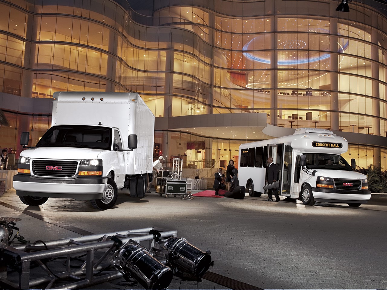 Two 2026 GMC Savana Cutaway Vans Parked Outside of a Concert Hall at Night