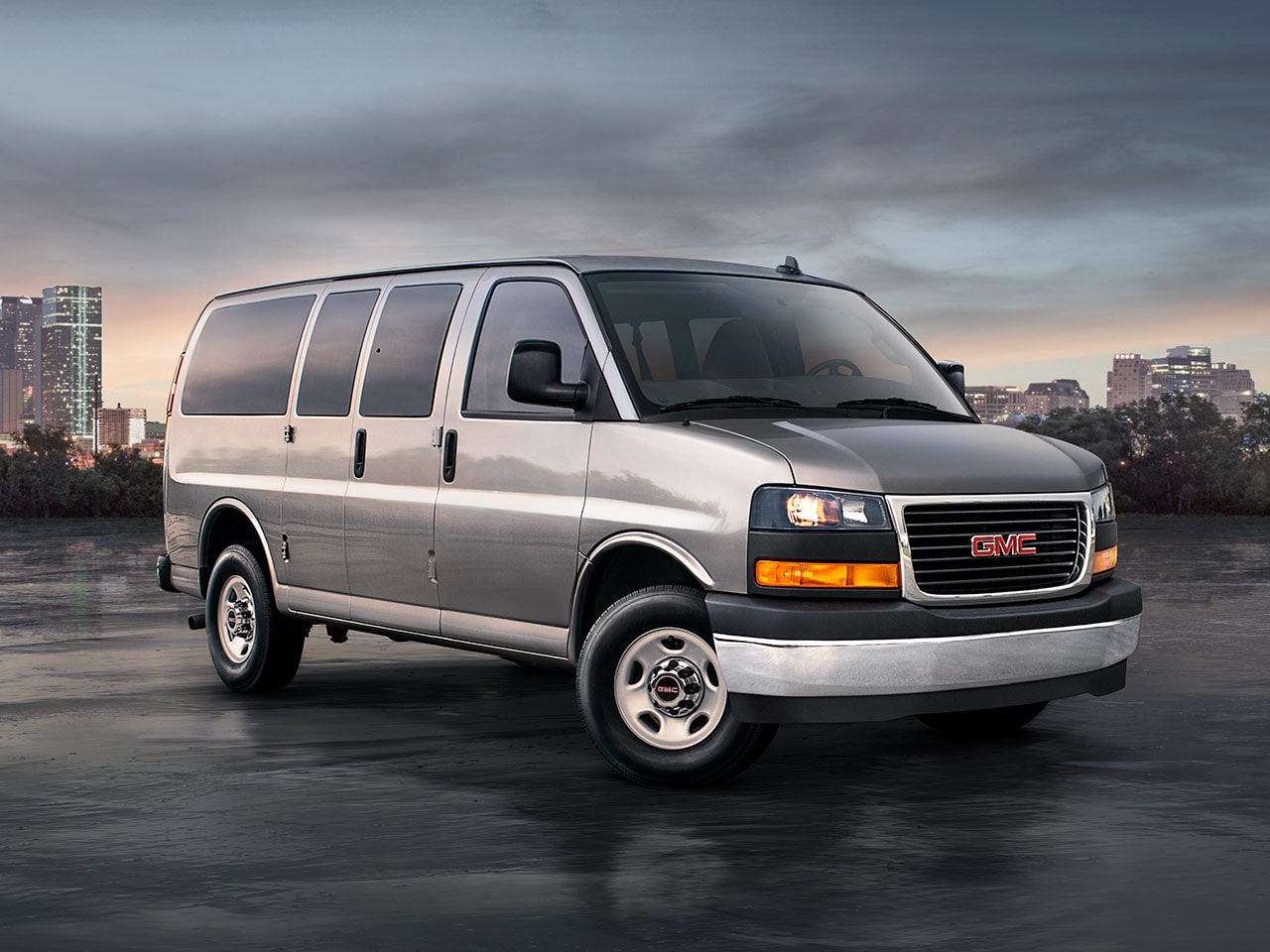 Wide Front Three-Quarters View of a 2026 GMC Savana Passenger Van with a City in the Background