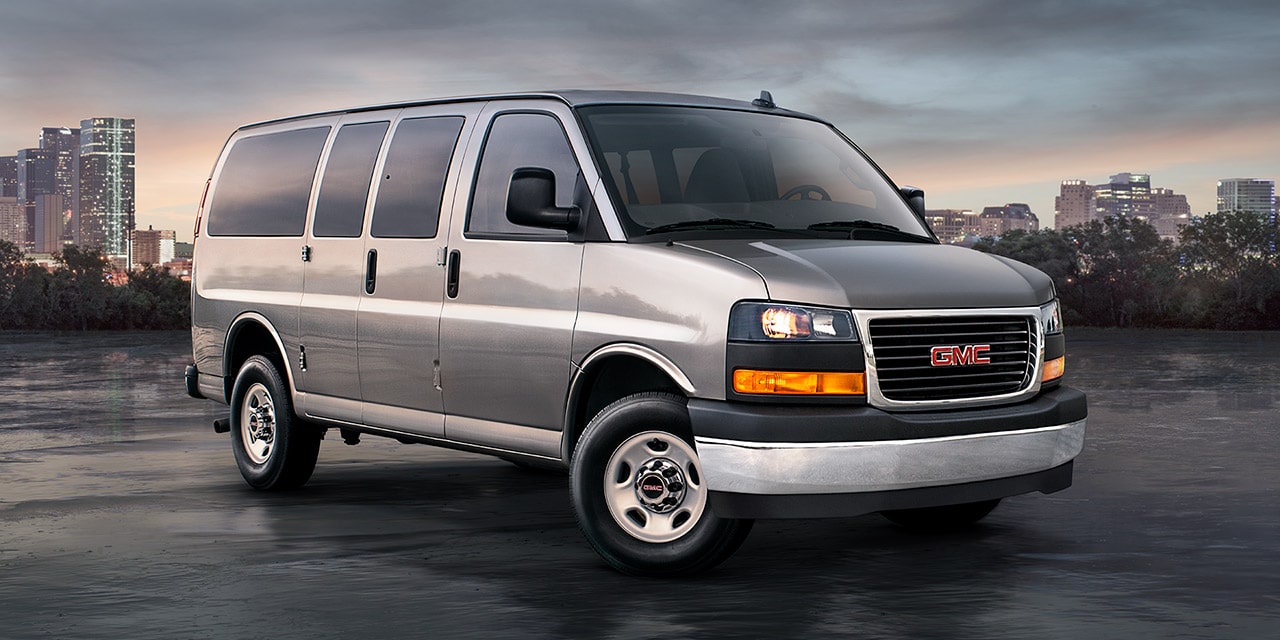 Front Three-Quarters View of a 2026 GMC Savana Passenger Van with a City in the Background