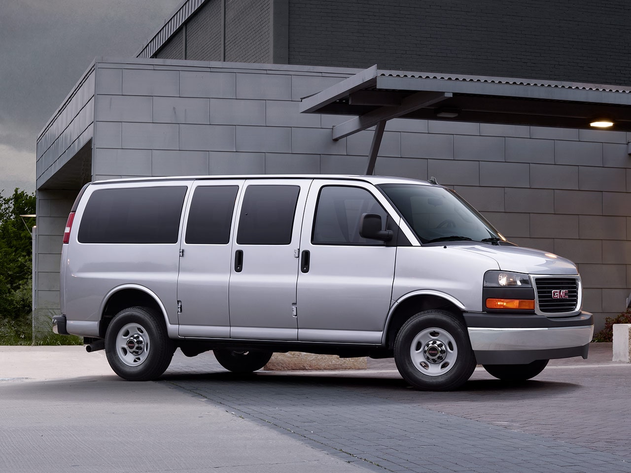 Wide Front Three-Quarters View of a 2026 GMC Savana Passenger Van with a Building in the Background
