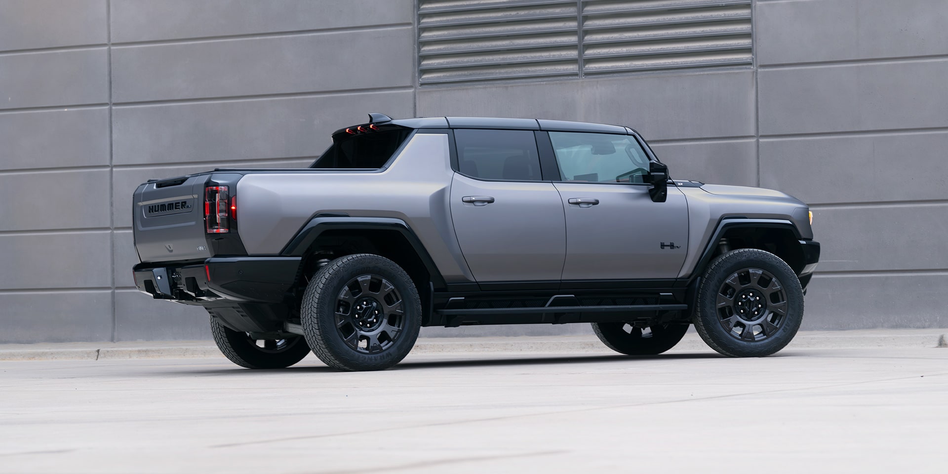 Rear Passenger Side View of the GMC HUMMER EV Pickup Truck Parked by a Concrete Wall