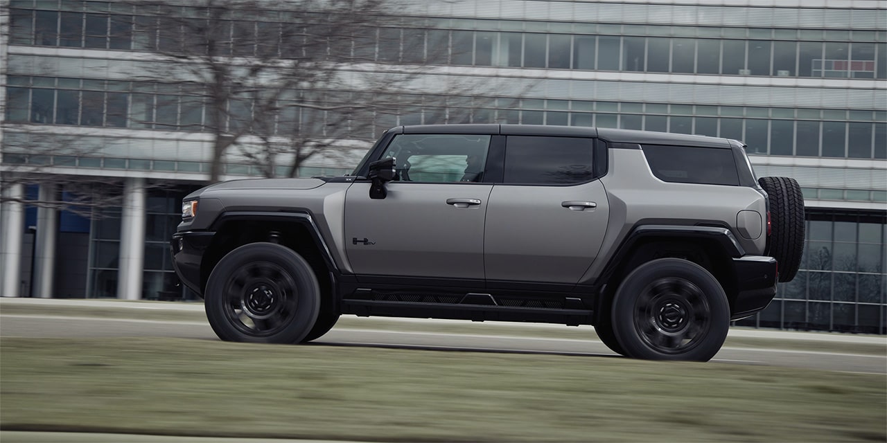 Blurry Driver Side View of the 2026 GMC HUMMER EV SUV Driving Past a Building