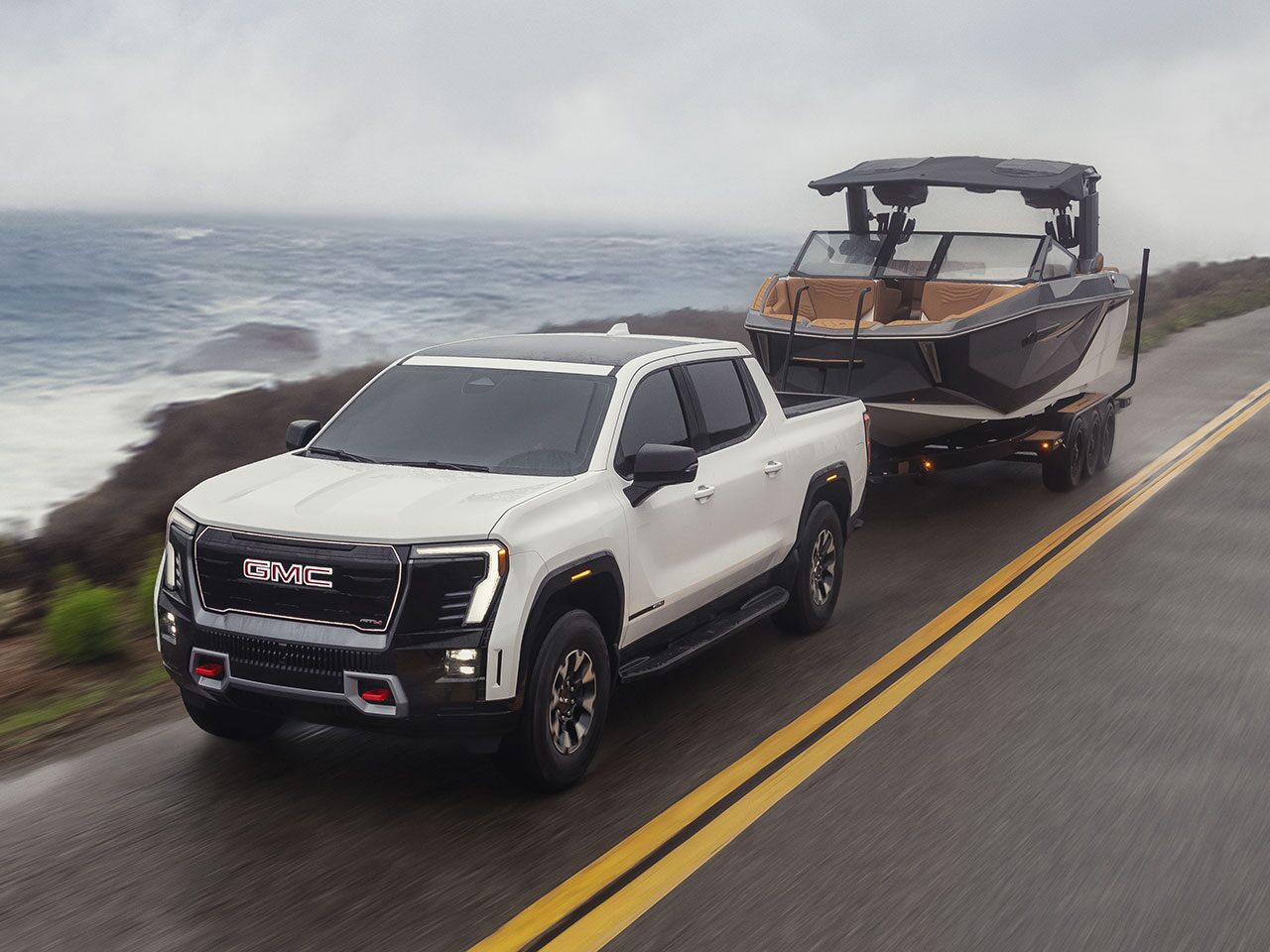 The 2026 GMC Sierra EV AT4 Pickup Truck Pulling a Boat Along a Road on the Coast