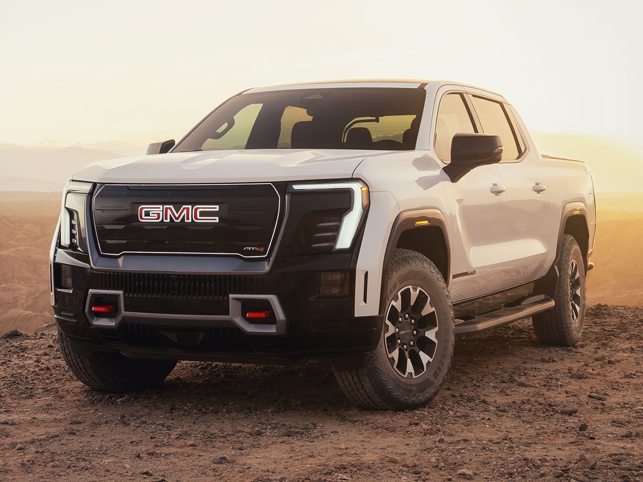 Front Three-Quarters View of the 2026 GMC Sierra EV AT4 Parked in the Desert at Sunset