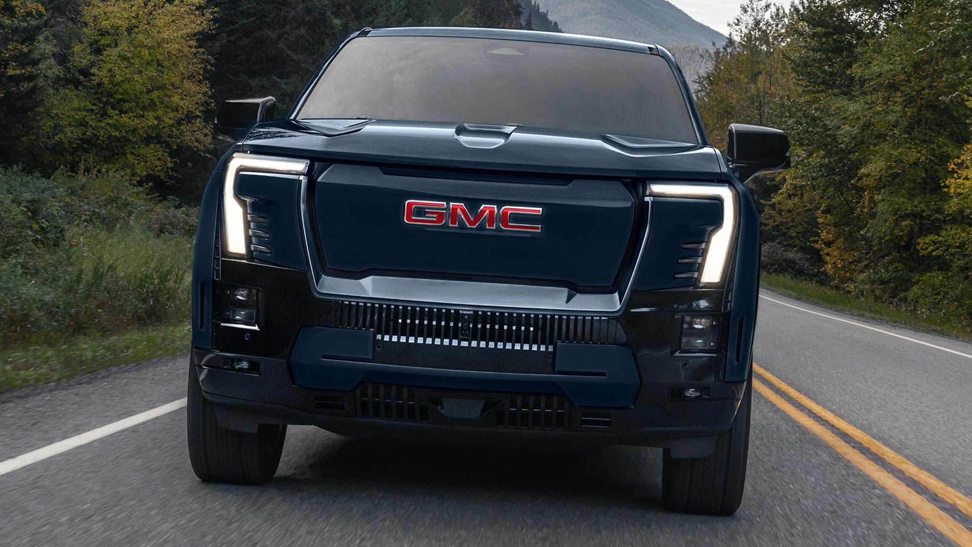 Front View of the 2026 GMC Sierra EV Denali Speeding Down the Tree Lined Road