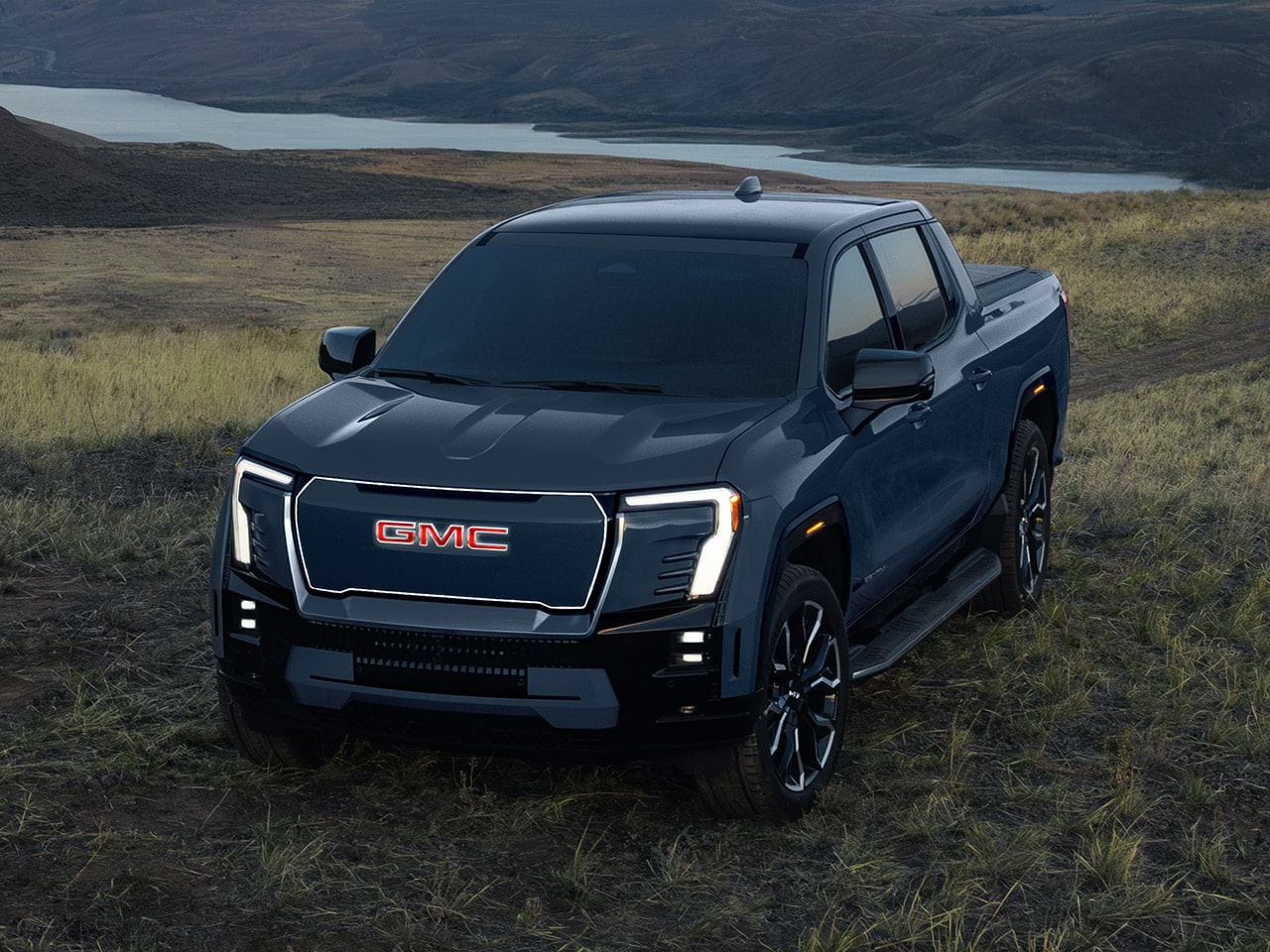 The 2026 GMC Sierra EV Denali Parked in a Field at Dusk with its Front Headlamps on