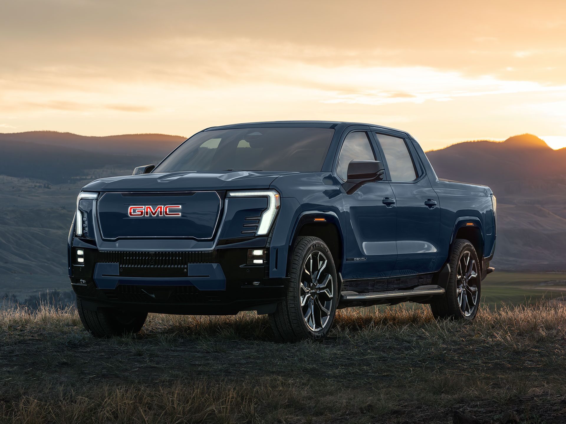 Front Three-Quarters View of the 2026 GMC Sierra EV Denali Parked in a Field at Sunset