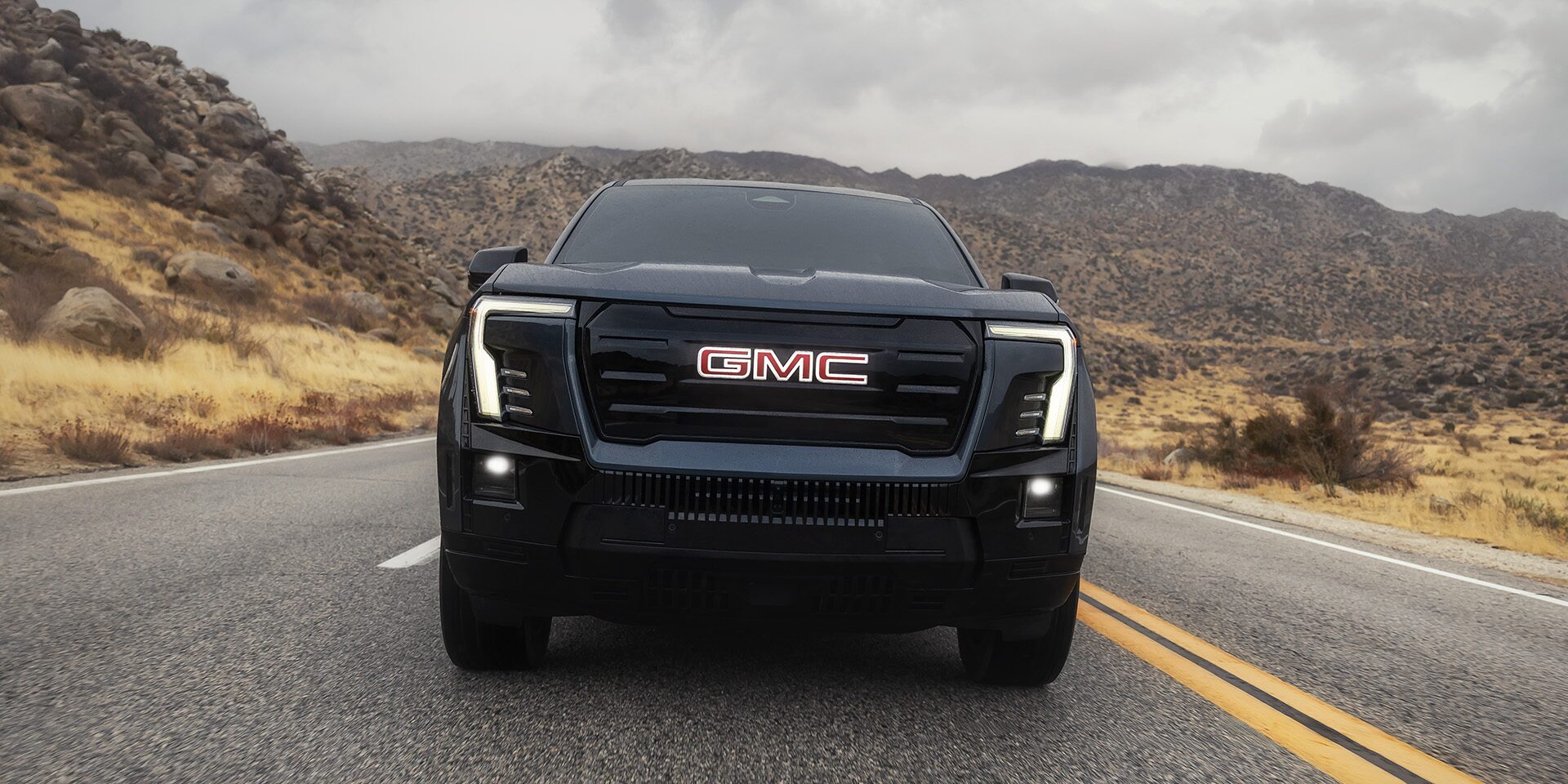 Front View of the 2026 GMC Sierra EV Elevation Driving Down the Open Road with a Mountain Range in the Distance