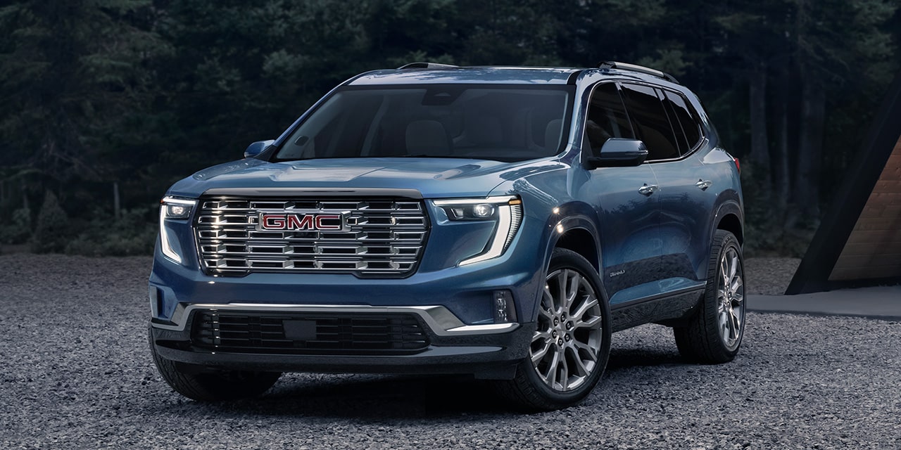 Front Three-Quarters View of a Blue 2026 GMC Acadia Denali Luxury Mid-Size SUV Parked in the Woods