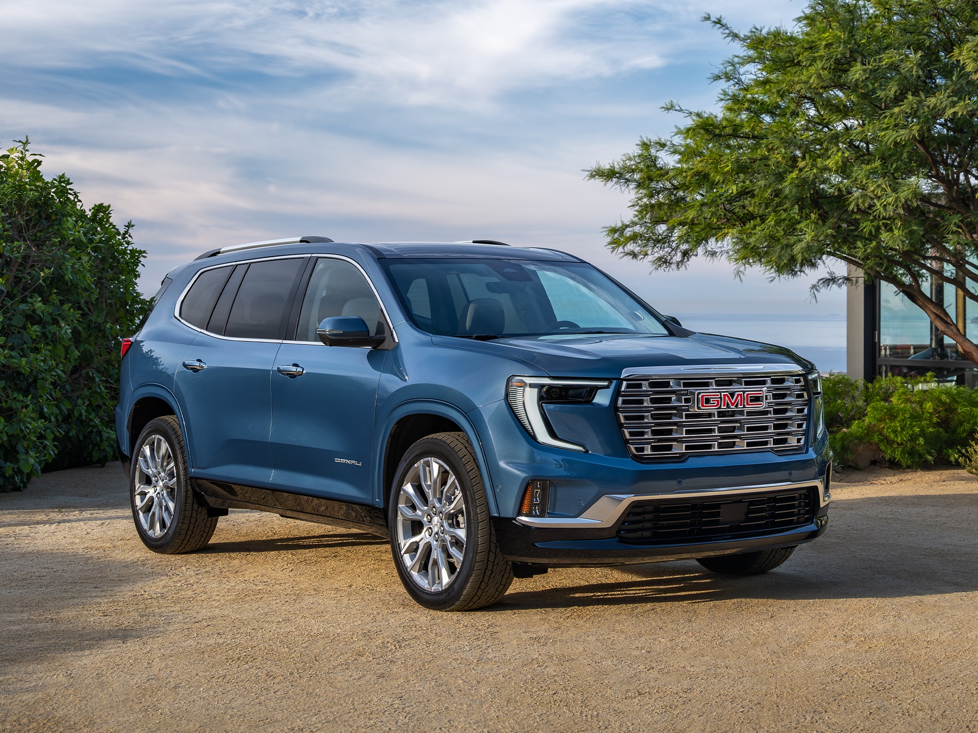 Front Three-Quarter View of the 2026 GMC Acadia Denali Luxury Mid-Size SUV with Beautiful Blue Skies in the Distance