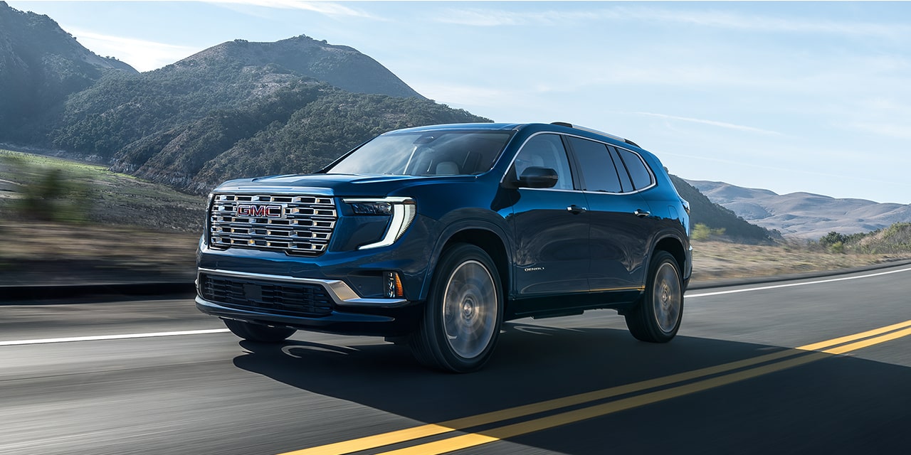 The 2026 GMC Acadia Denali Mid-Size SUV Driving Down a Road Lined with Beautiful Mountains