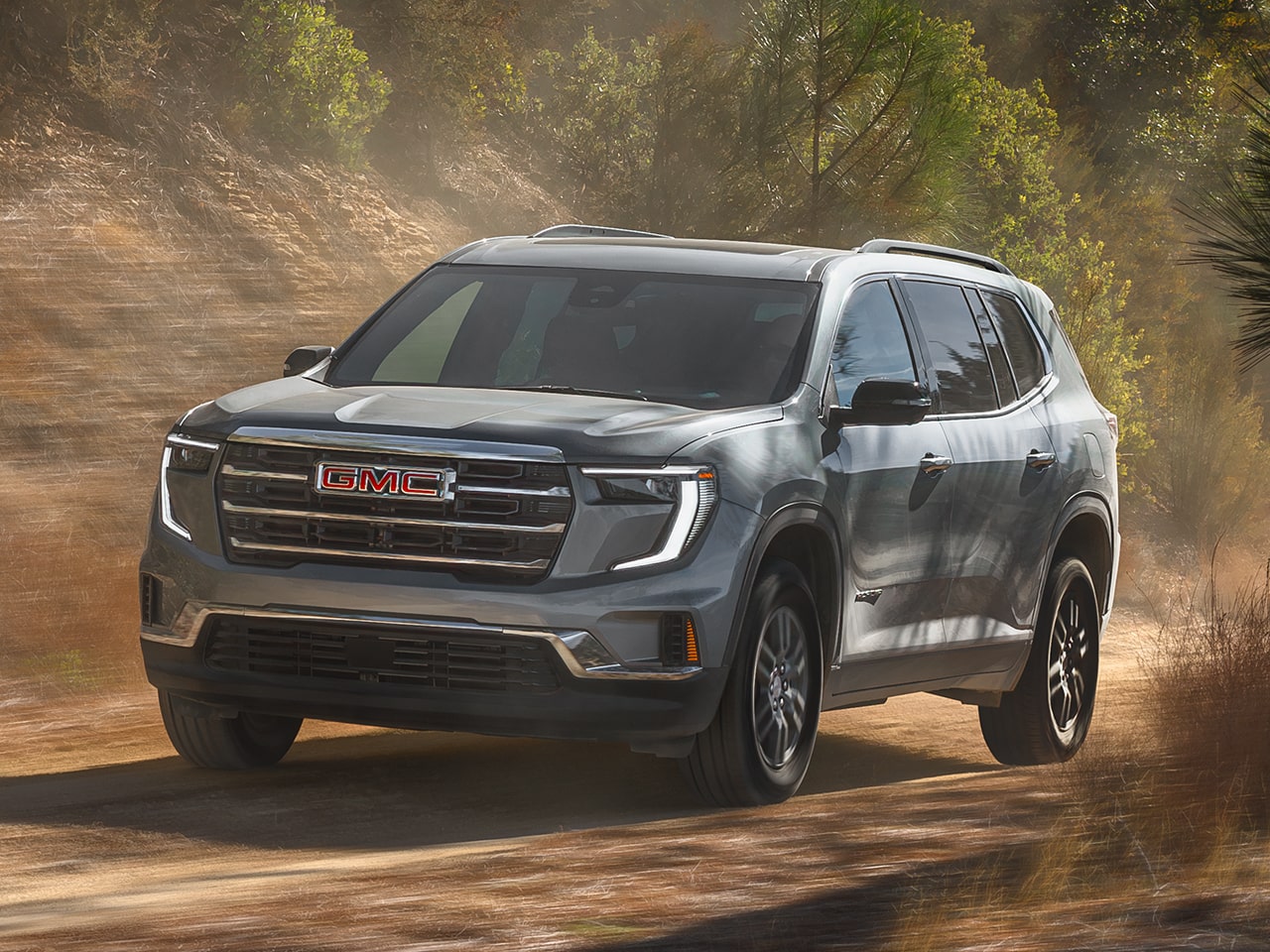 Front Three-Quarters View of a 2026 GMC Acadia Elevation Mid-Size SUV Driving Down a Dirt Road